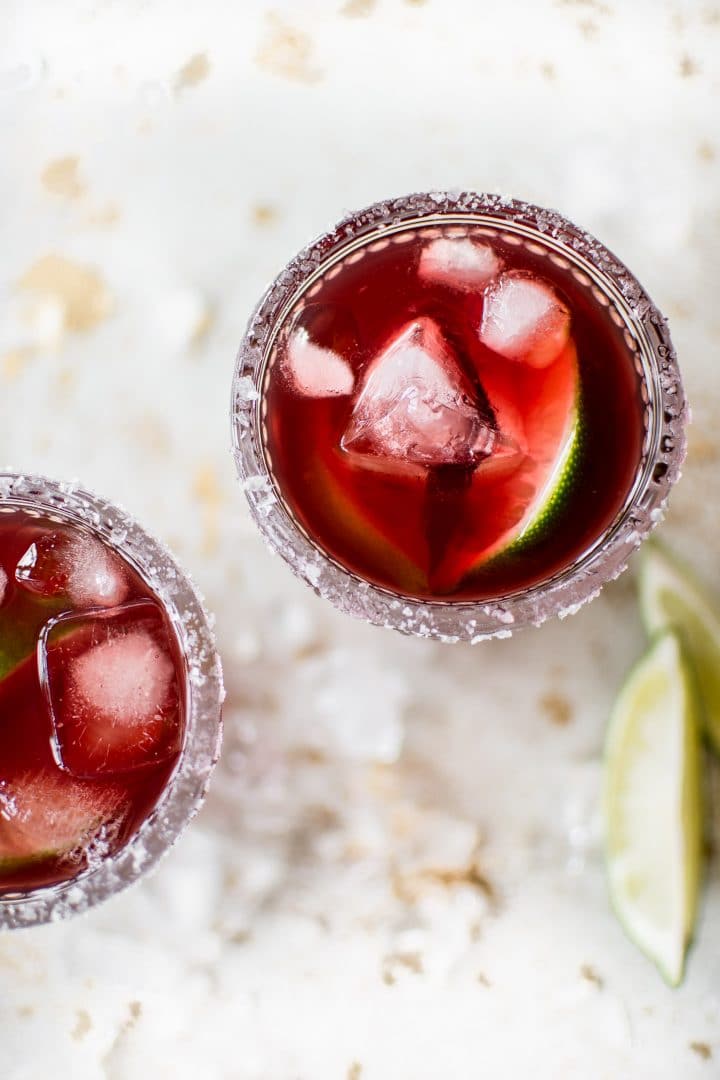 pomegranate margarita with ice in a glass and limes beside it