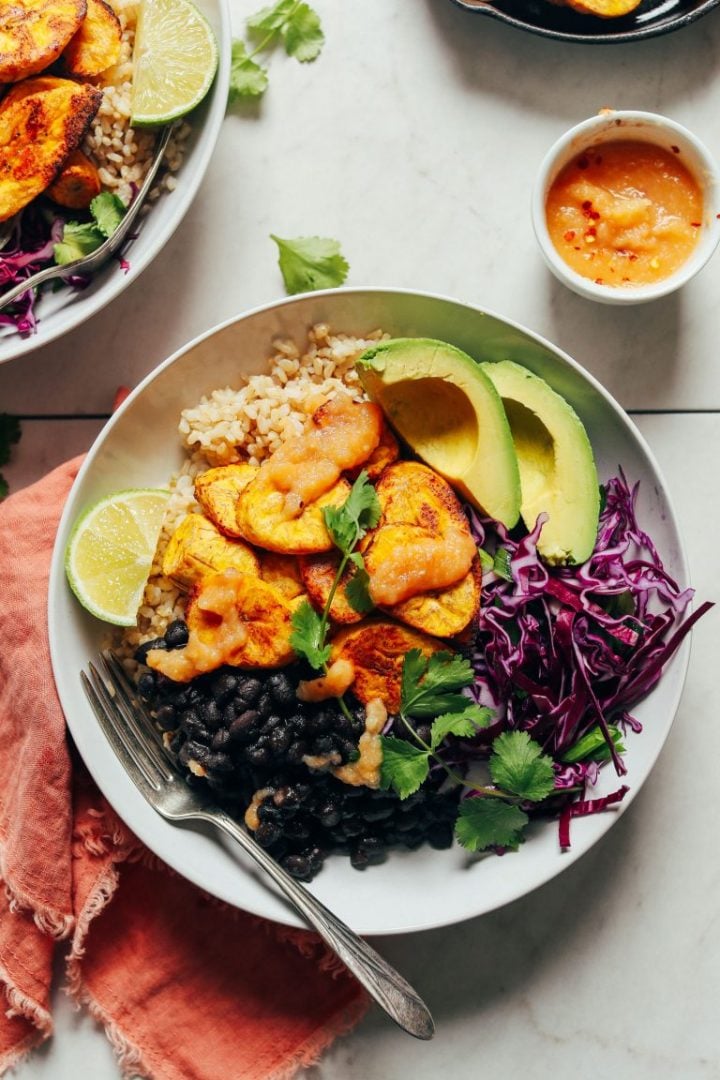 vegan plantain and black bean bowl with a fork, avocado, and lime wedge
