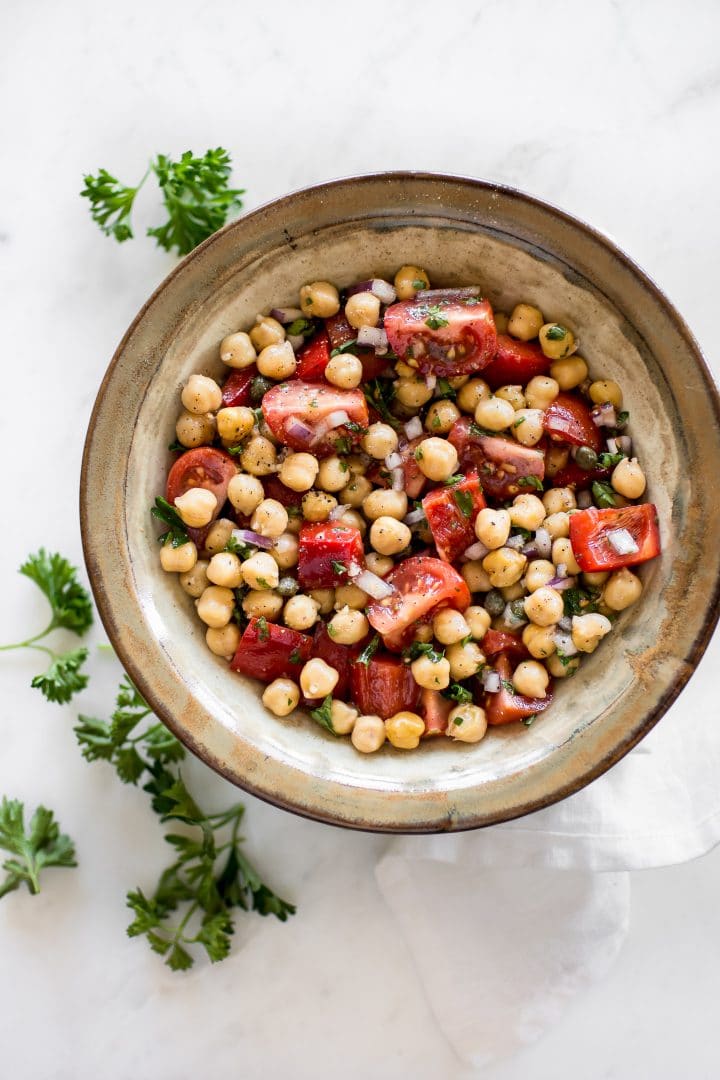 bowl of healthy chickpea and tomato salad beside parsley sprigs