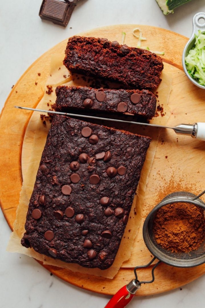 chocolate zucchini bread loaf with a knife slicing it on a wooden cutting board