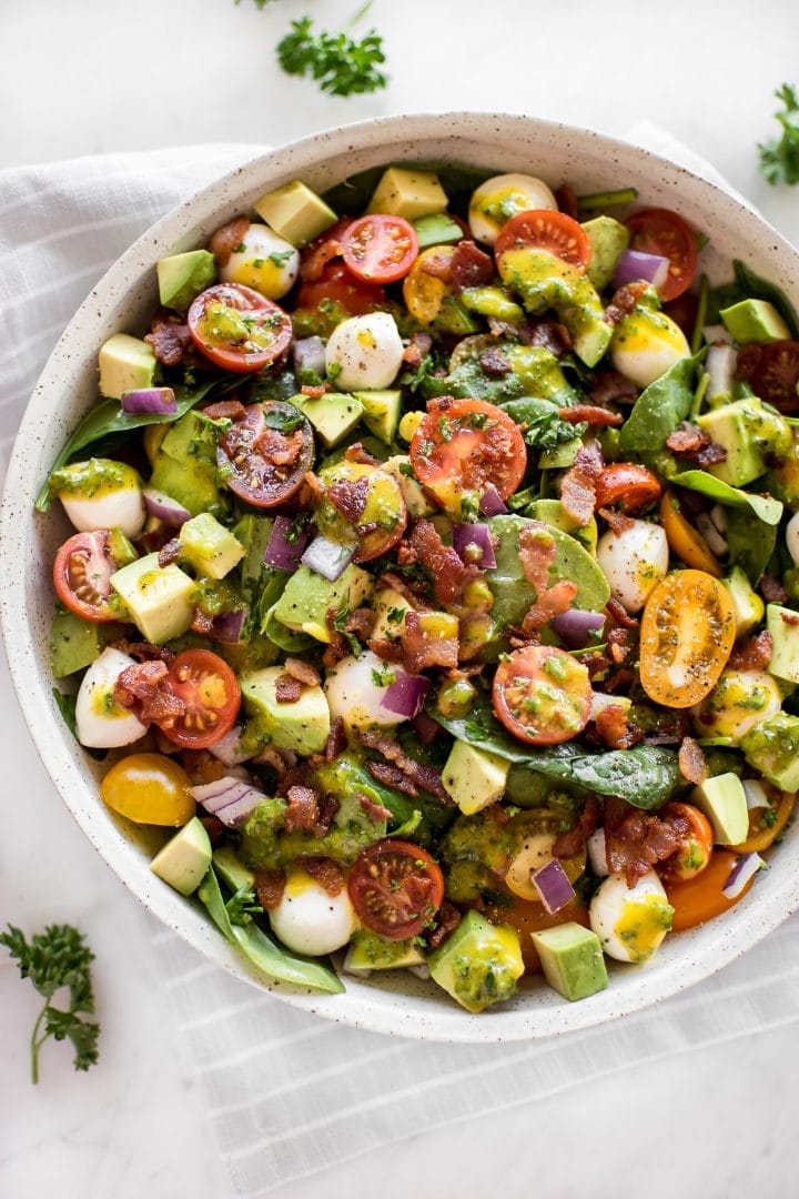 avocado bacon salad with honey mustard dressing in beige bowl and parsley garnish