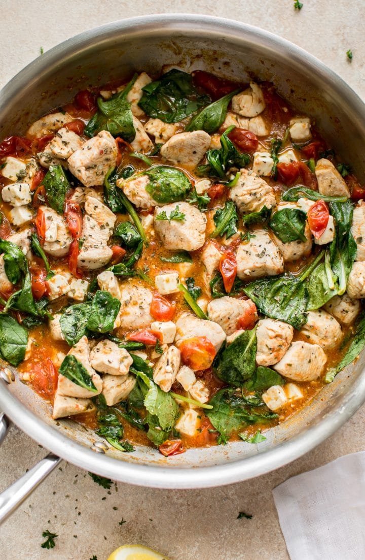 chicken, spinach, tomatoes cooking in a metal skillet