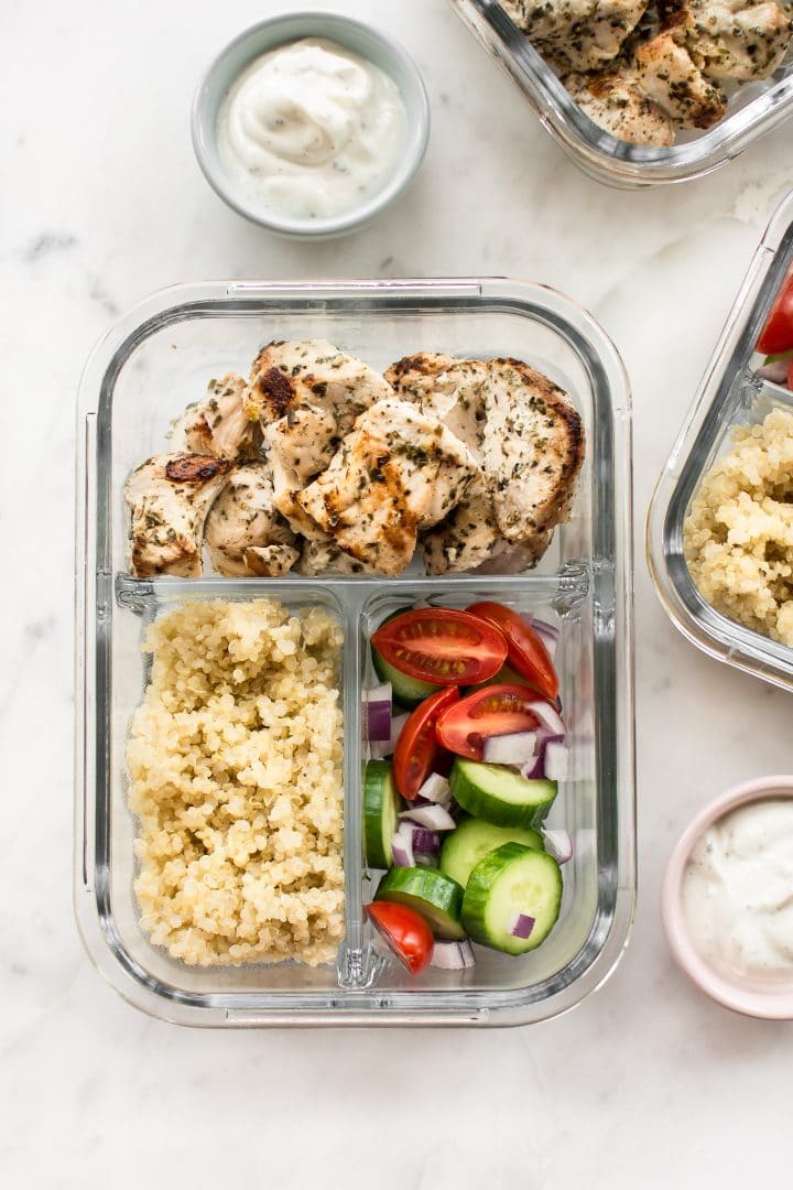 close-up of glass meal prep container with grilled chicken souvlaki with quinoa and vegetables