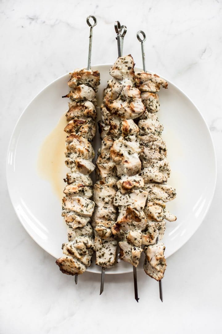 white plate with four grilled chicken skewers