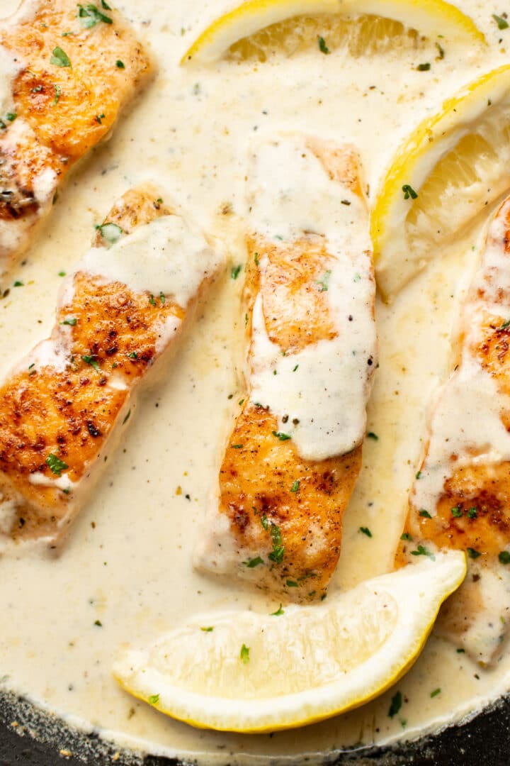 closeup of creamy lemon salmon in a skillet with lemon wedges