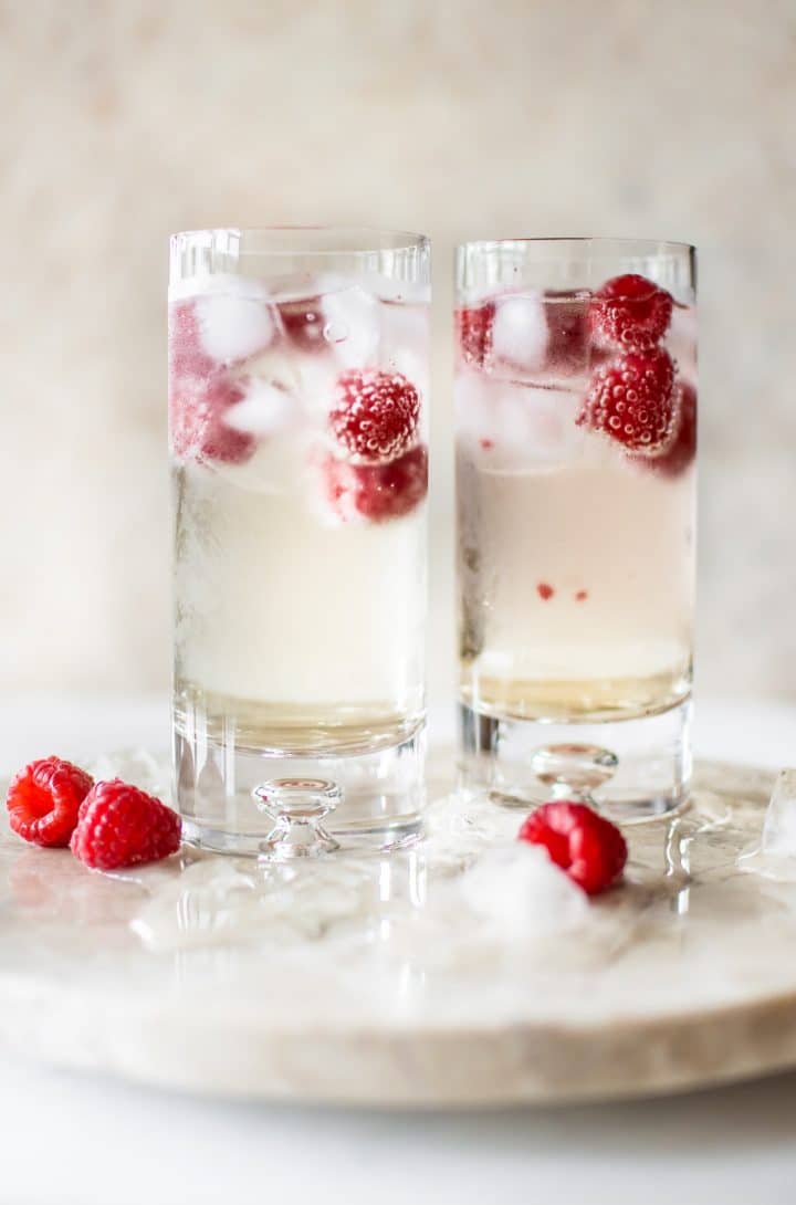 two glasses of sparkling elderflower alcohol-free drink with ice and raspberries
