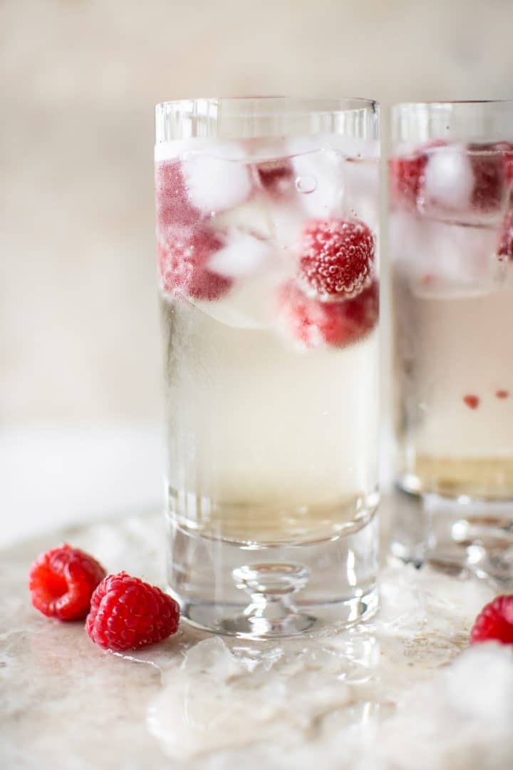 two glasses of elderflower mocktail with ice cubes and raspberries