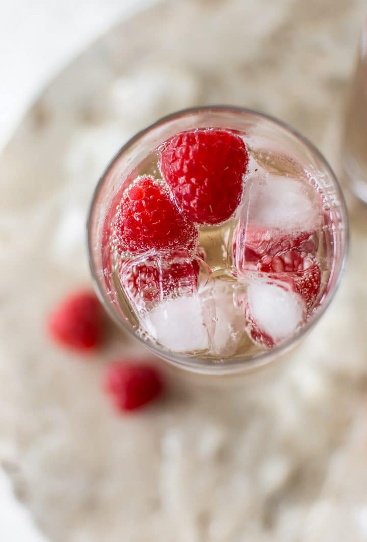 close-up of a glass of sparkling elderflower mocktail with ice cubes and raspberries