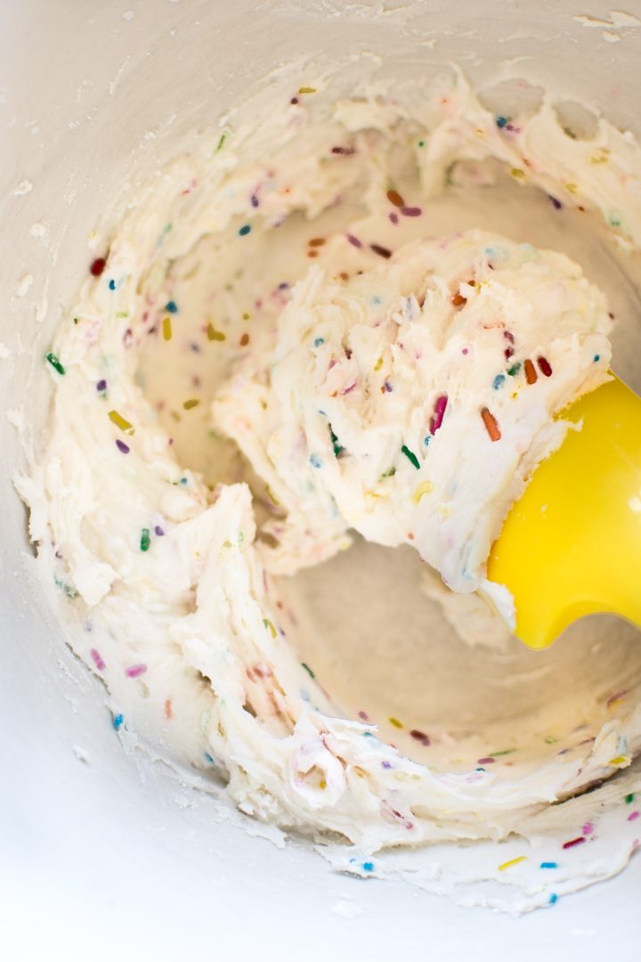 close-up of rainbow sprinkles frosting in a mixing bowl with spatula