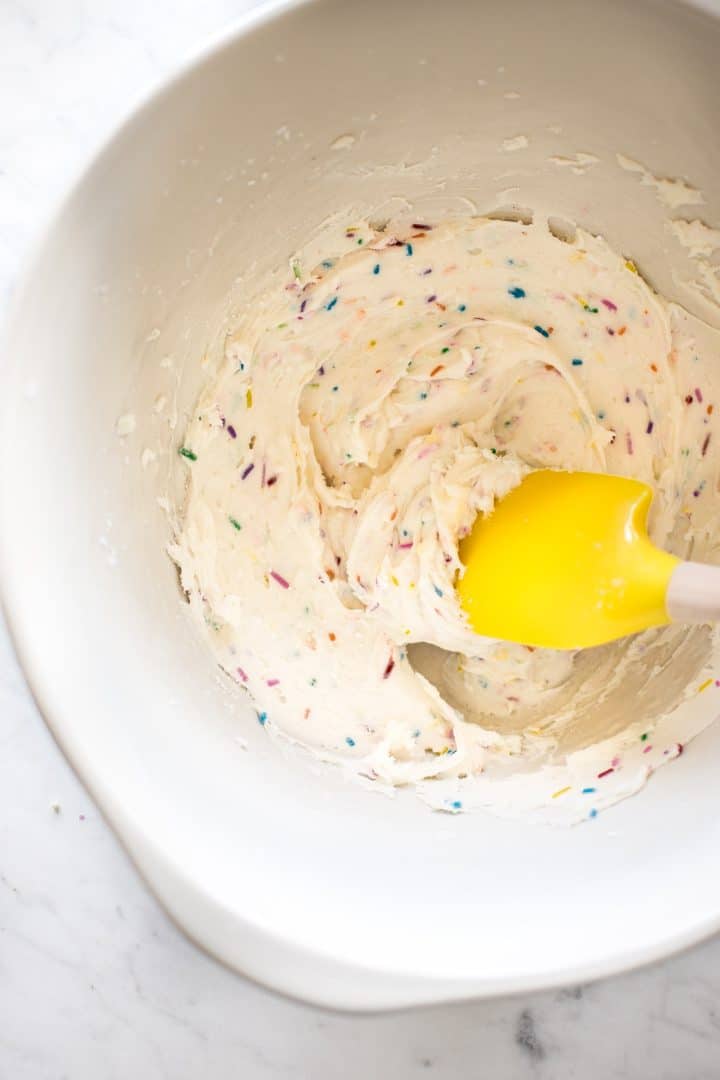 funfetti frosting in a white mixing bowl with a spatula