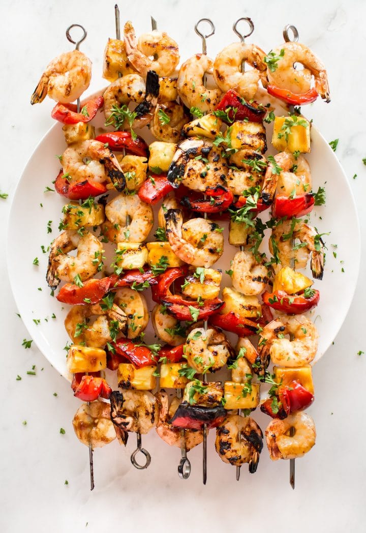 several Hawaiian grilled shrimp skewers with red peppers on a white plate
