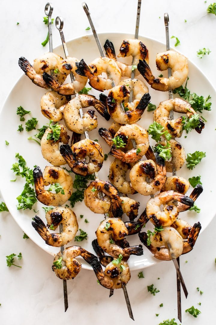 several honey garlic grilled shrimp skewers on a plate with parsley garnish