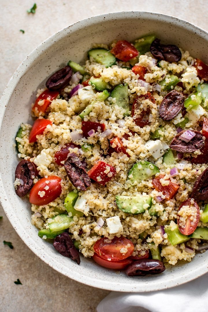 Mediterranean quinoa salad with tomatoes, feta, and olives in a beige bowl