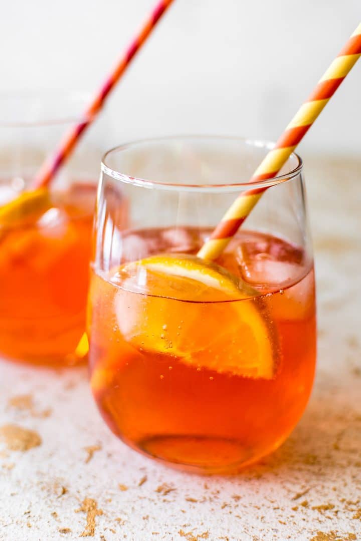 a glass of aperol spritz cocktail with a slice of lemon and a straw