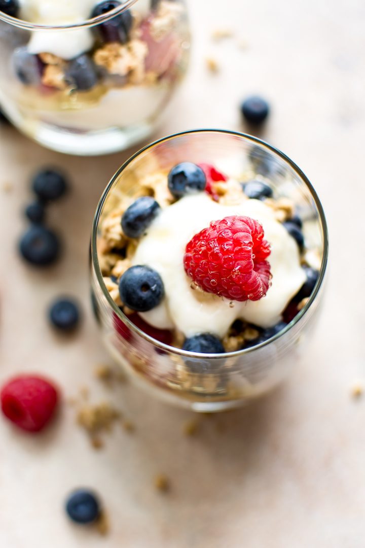 close-up of berry breakfast parfait in a glass with a raspberry on a dollop of yogurt