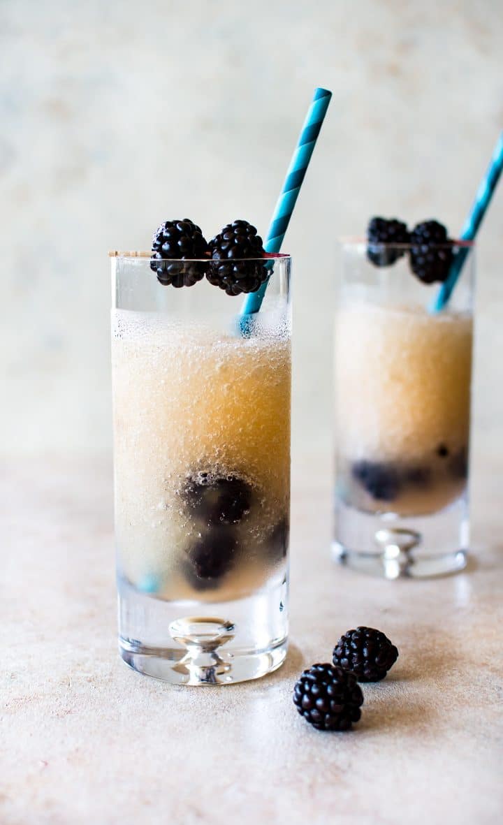two clear glasses with blackberry frozen riesling and blue striped paper straws and garnished with blackberries