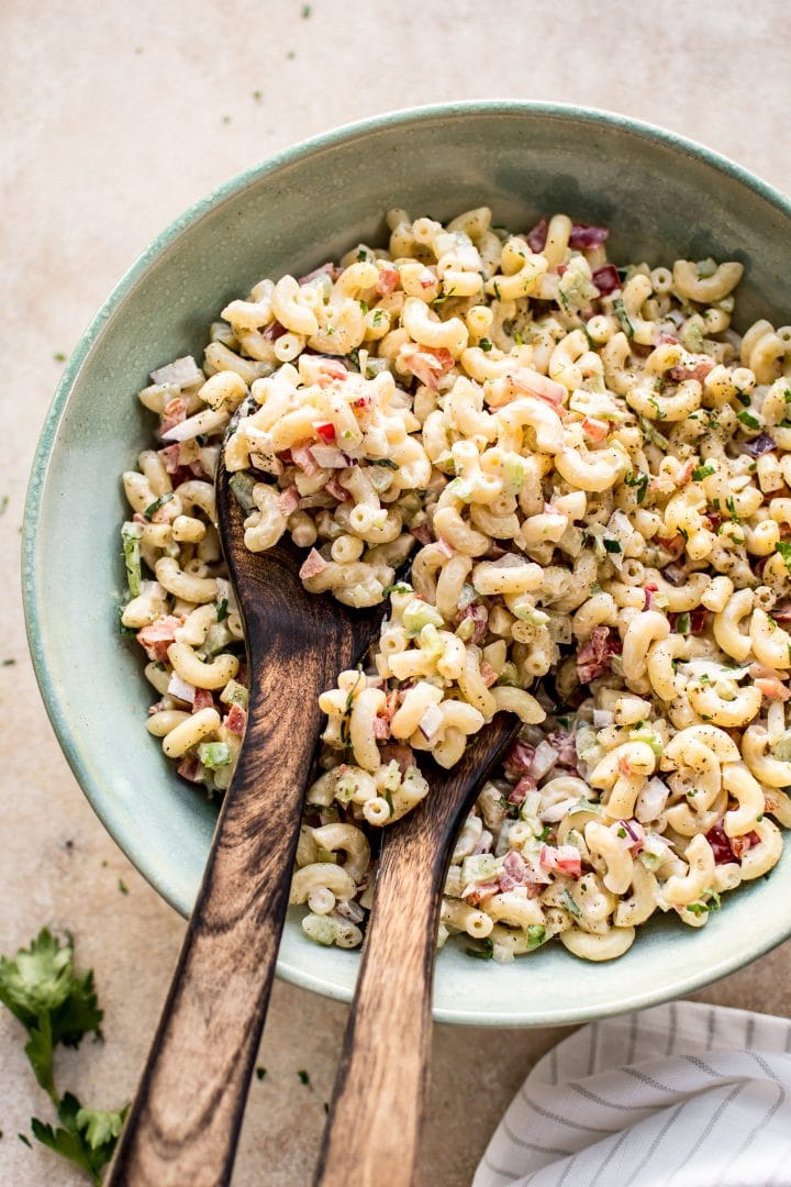 creamy macaroni salad in a teal bowl with wooden salad utensils