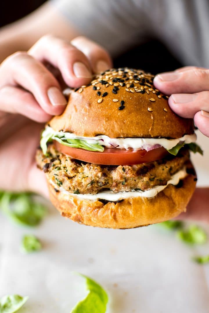 close-up of a man holding a ground turkey burger with mayo, tomato, and lettuce on a sesame bun