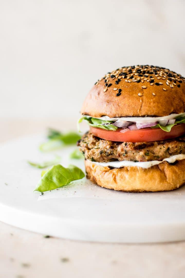 ground turkey burger on a white cutting board with lettuce and tomatoes