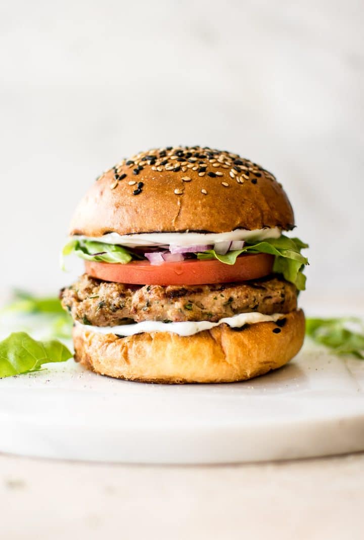 healthy ground turkey burger with tomato, lettuce, and mayo on a sesame bun on a white cutting board