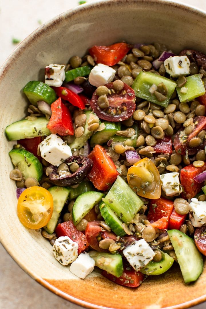 close-up of cucumbers, feta, peppers, tomatoes, and lentils in mediterranean salad in an earthenware bowl