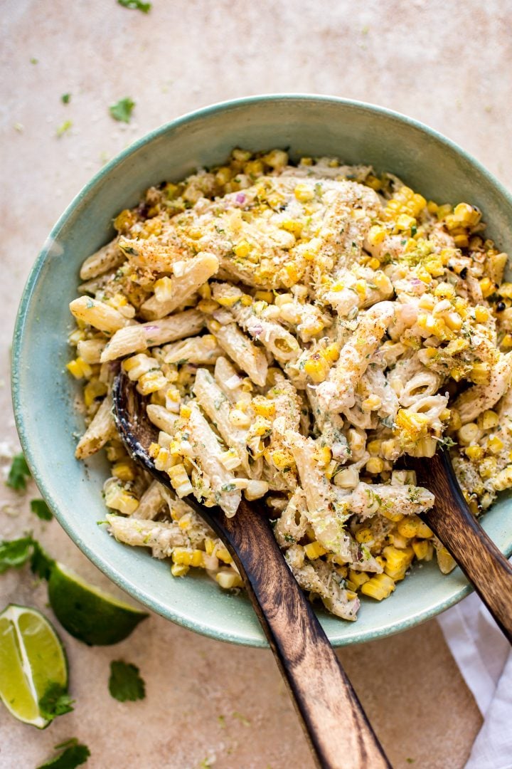 Mexican street corn pasta salad in a teal bowl with wooden salad utensils