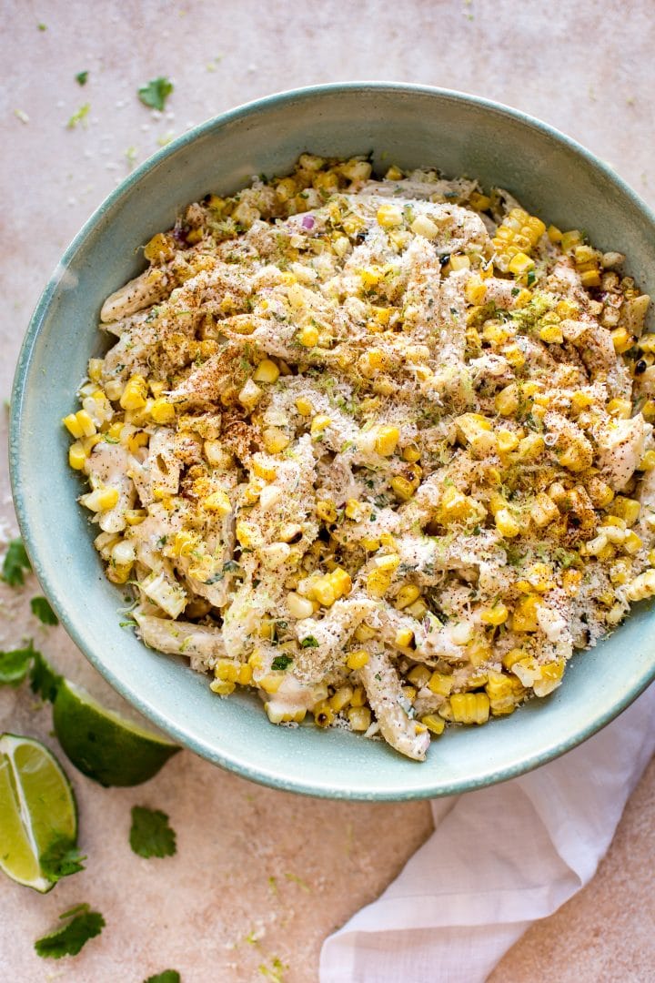 Mexican street corn pasta salad in a teal bowl beside lime wedges