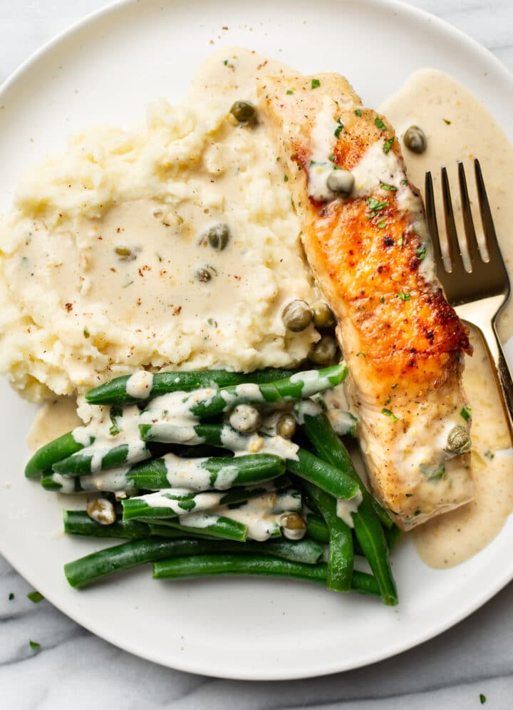 a plate with salmon piccata, mashed potatoes, and green beans