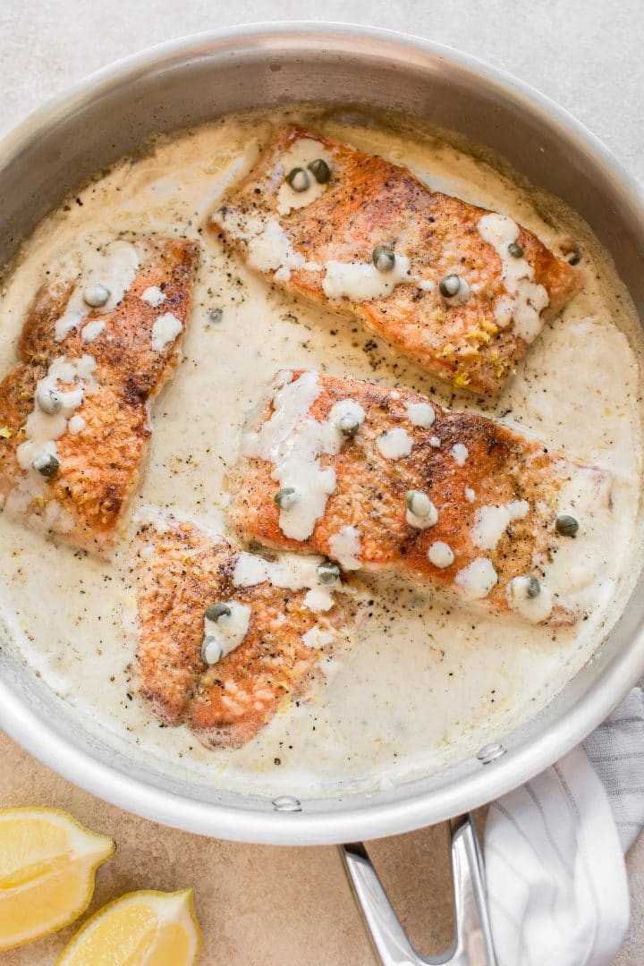 salmon in a creamy piccata sauce in a metal skillet
