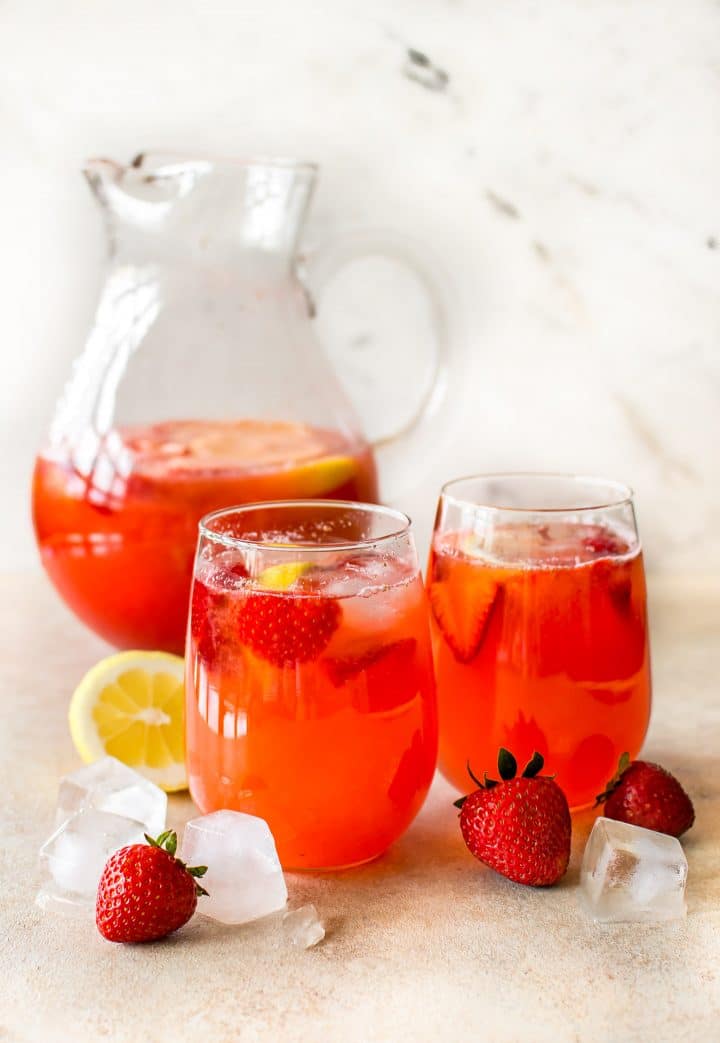 glass pitcher of strawberry lemonade beside two glasses of lemonade