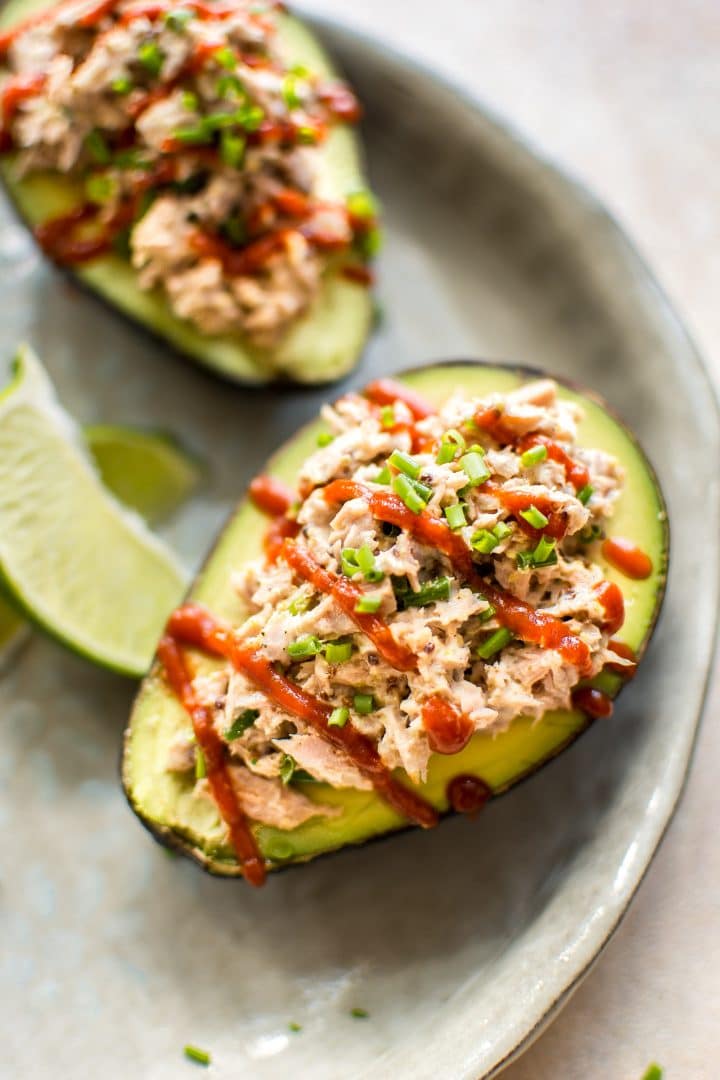 spicy tuna stuffed avocado with sriracha drizzle beside lime wedges