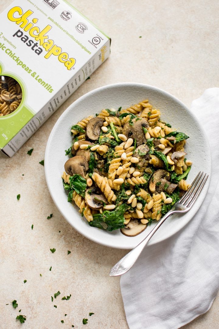 vegan mushroom spinach pasta on a white plate with a fork beside a box of Chickapea pasta