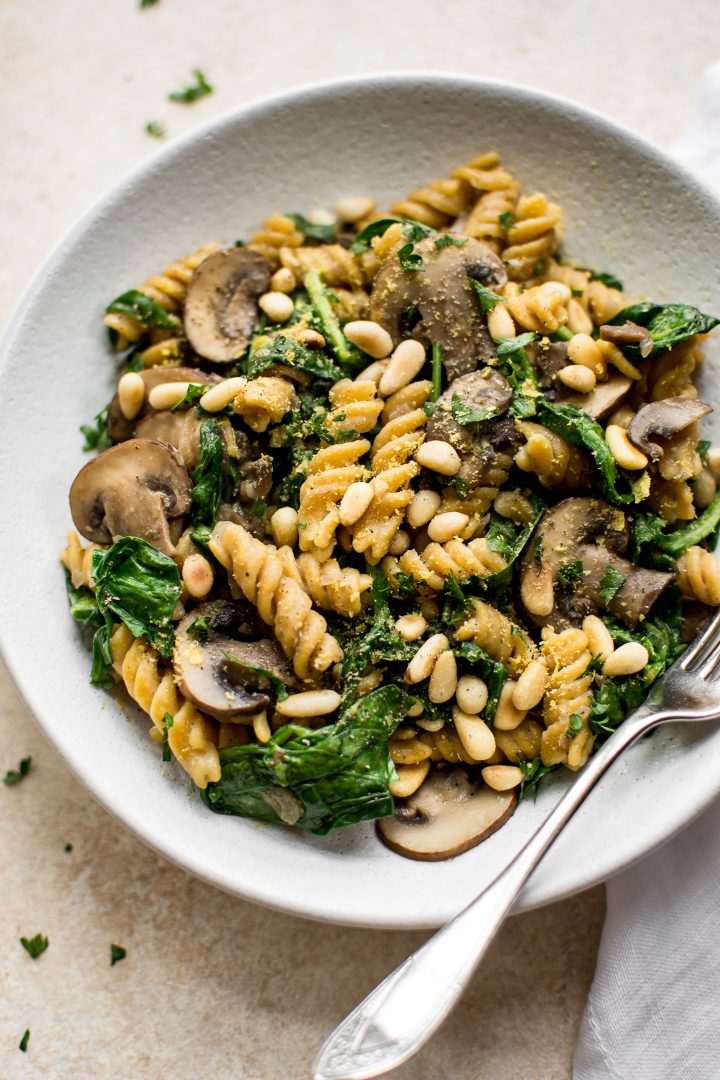 close-up of vegan spinach mushroom pasta on a white plate with a silver fork