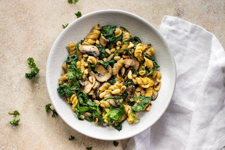 vegan spinach and mushroom pasta on a white plate beside a white cloth napkin