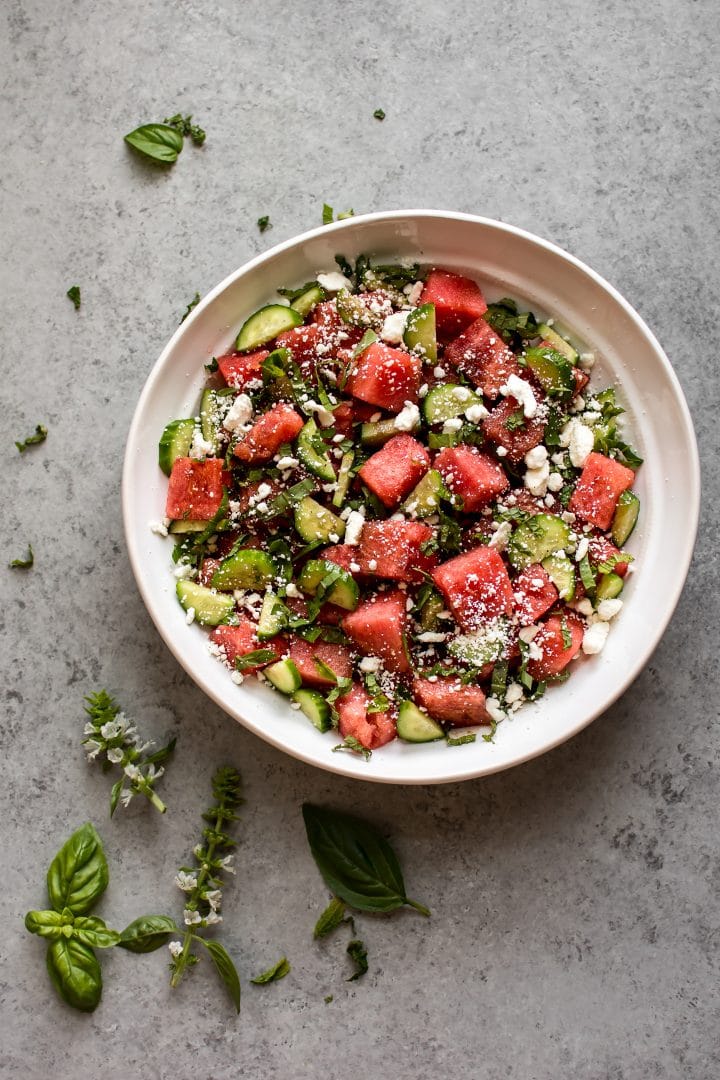 easy watermelon and feta salad in a white bowl on a grey surface with basil leaves