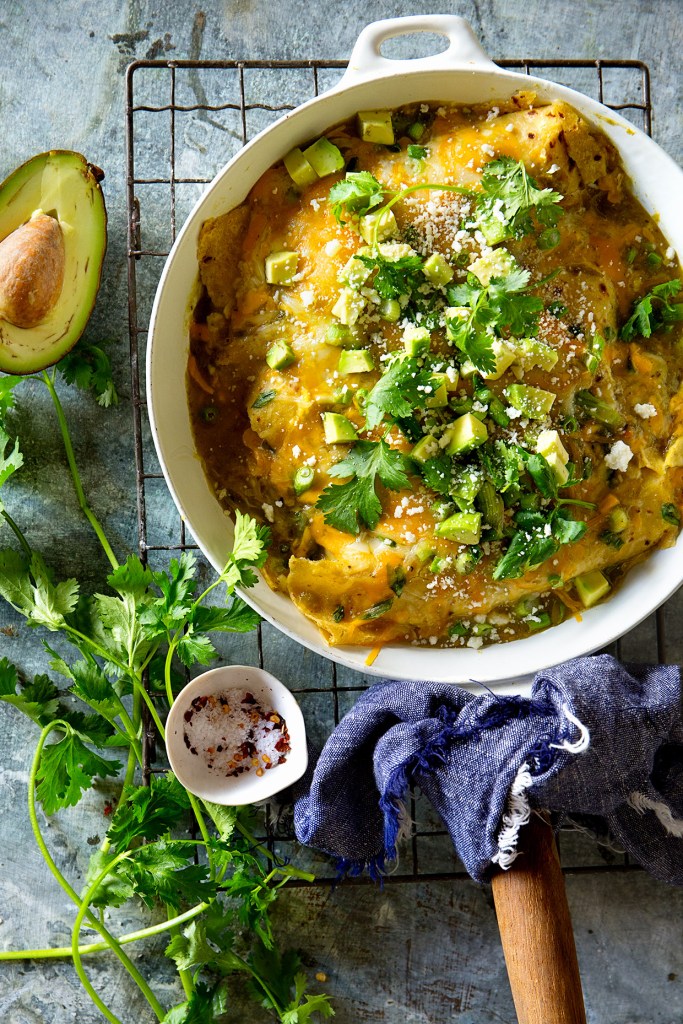 chicken verde enchiladas in a white pot on a wire rack with fresh herbs