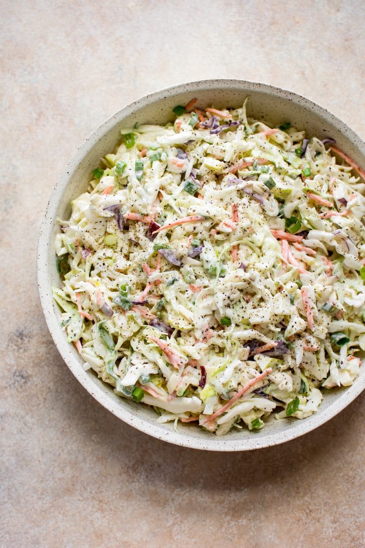 apple and cabbage slaw with creamy dressing in a beige bowl
