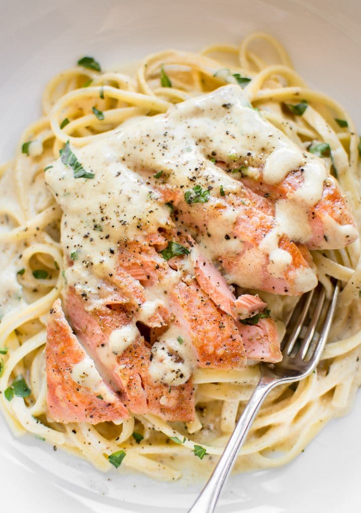close-up of creamy dijon salmon over pasta in a white bowl with a fork