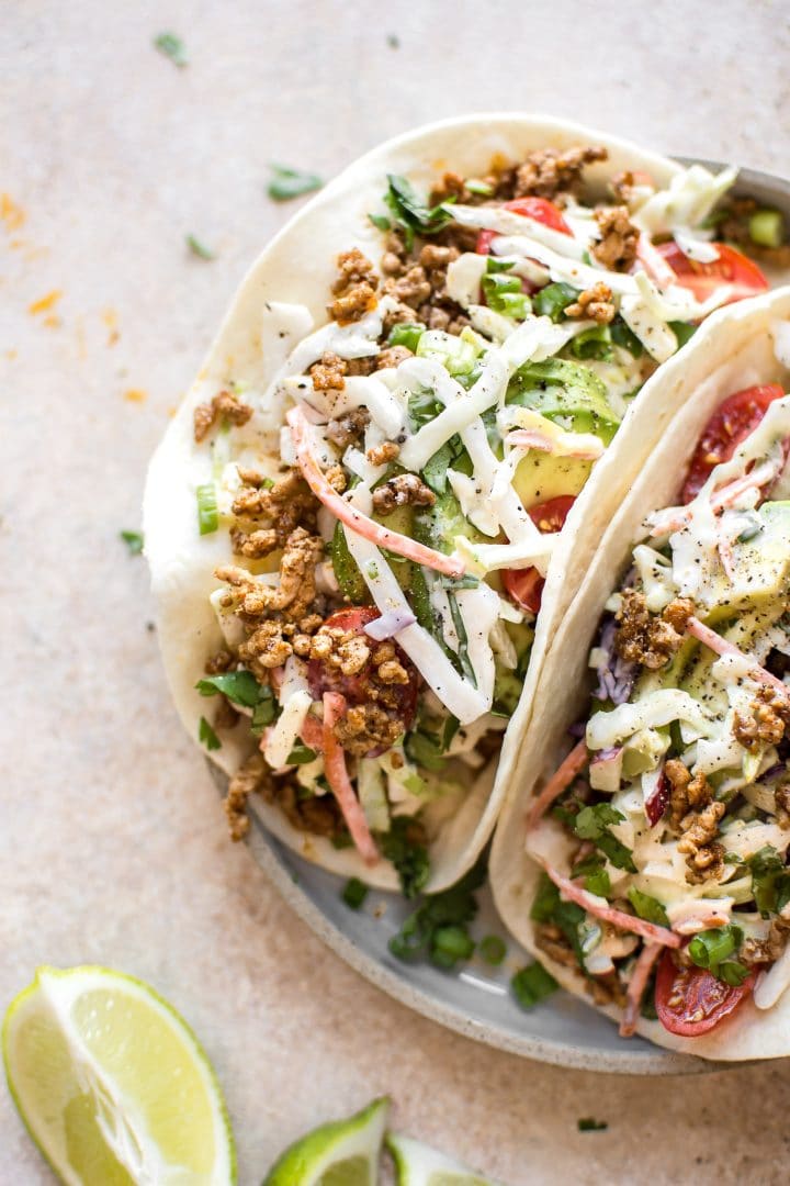 two ground pork tacos with homemade apple slaw on a plate with lime wedges