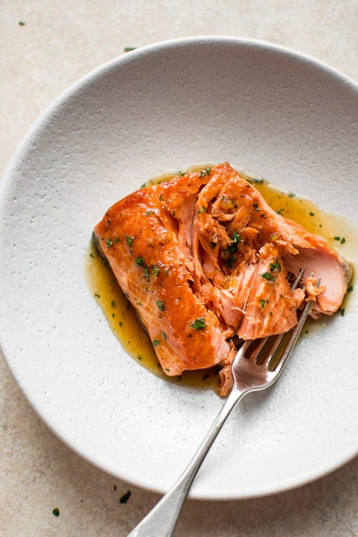 close-up of a piece of honey garlic salmon in a white bowl with a fork