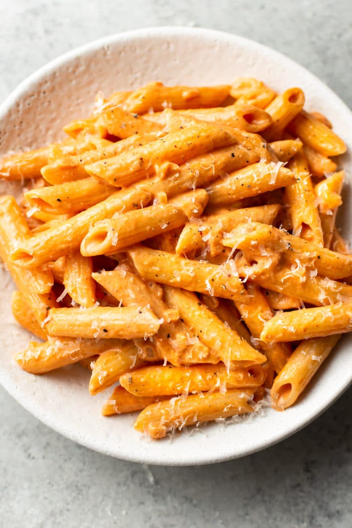 the best penne alla vodka in a white bowl with parmesan cheese grated on top