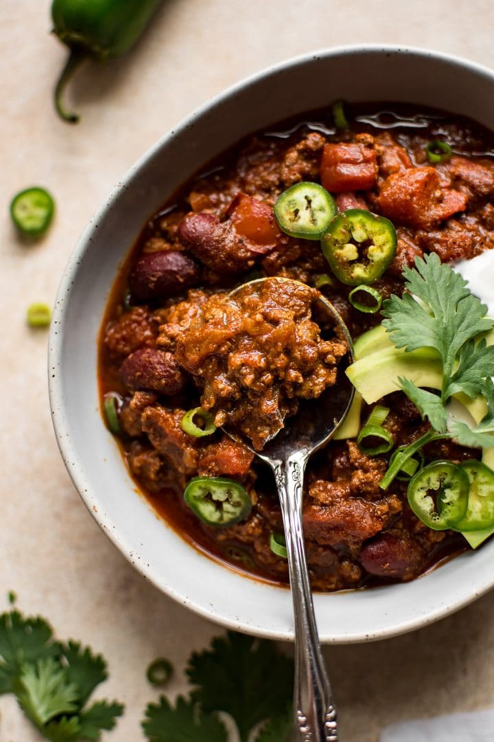 close-up of quick beef chili in a white bowl with avocado, sour cream, and parsley toppings