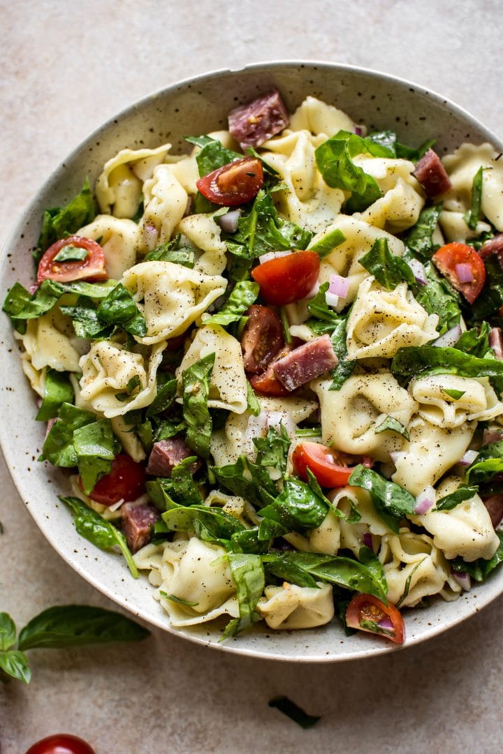 close-up of spinach and salami tortellini salad in a beige bowl