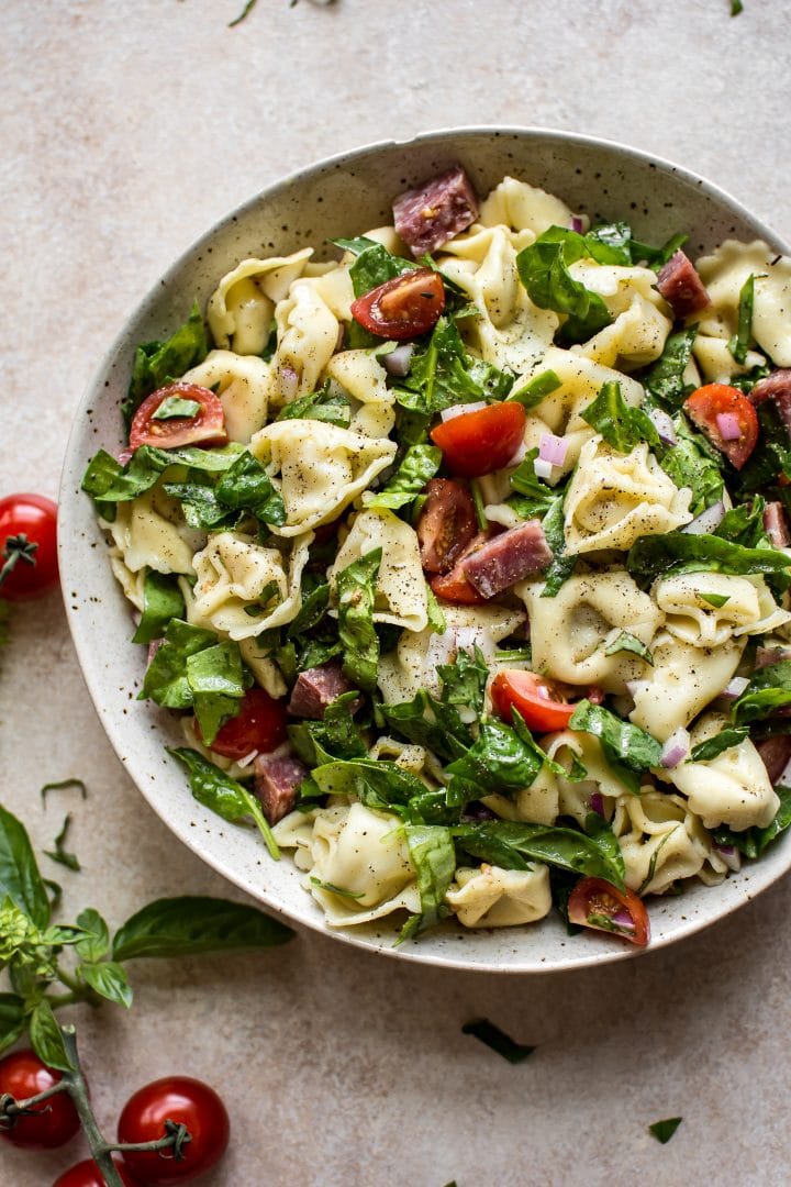 spinach tortellini pasta salad with salami, basil, and fresh tomatoes in a white bowl