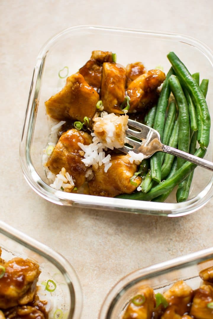 close-up of glass container with homemade mongolian chicken with rice and green beans and a fork