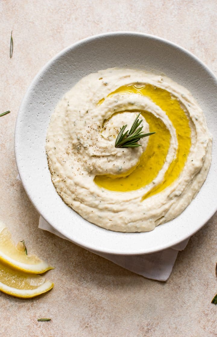 close-up of white bowl with easy cannellini bean dip and lemon slices