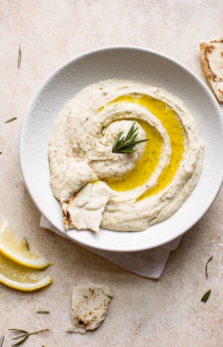 vegan white bean dip with rosemary, lemon juice, garlic, and good olive oil in a white bowl with pita bread