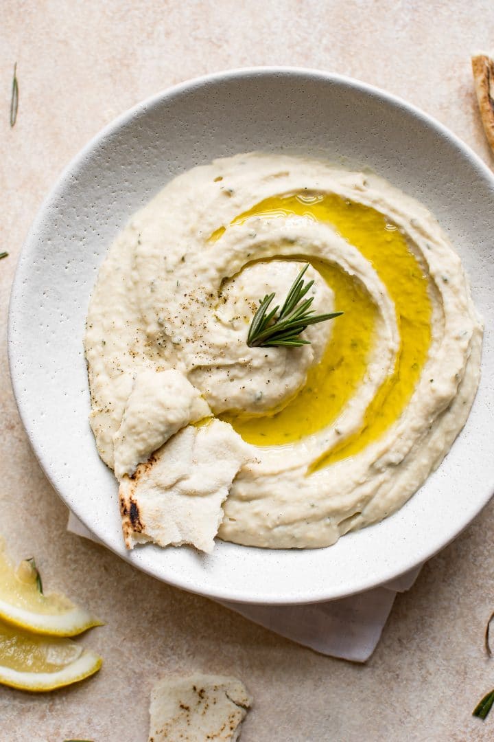 healthy white bean dip with rosemary in a white bowl with pita bread and lemon slices