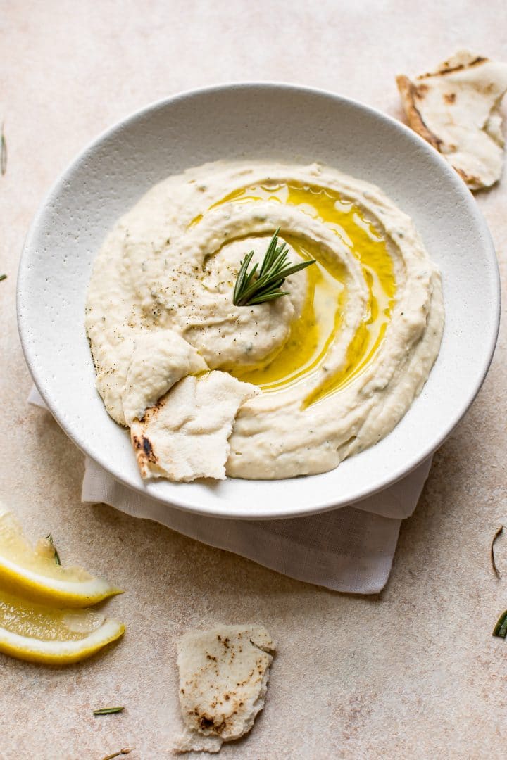 vegan white bean rosemary dip in a bowl with a sprig of rosemary and pita bread