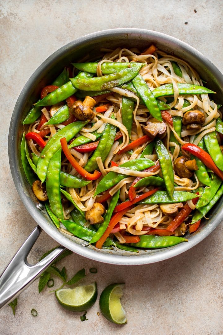 skillet full of vegan rice noodles with a sweet and spicy ginger garlic sauce and lime wedges